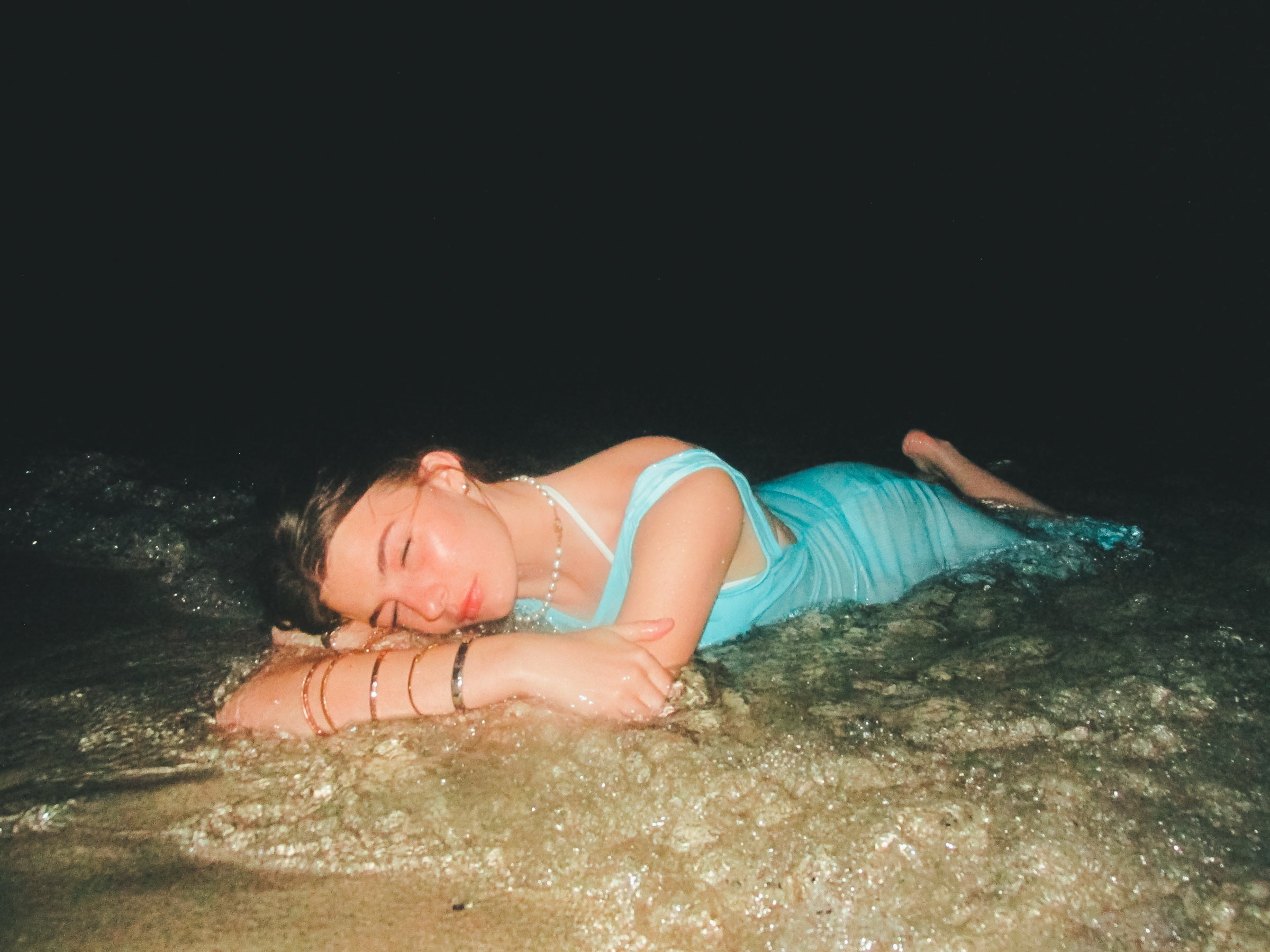 Woman in aqua sheer maxi dress lying in ocean waves at night — beach cover up style 2026